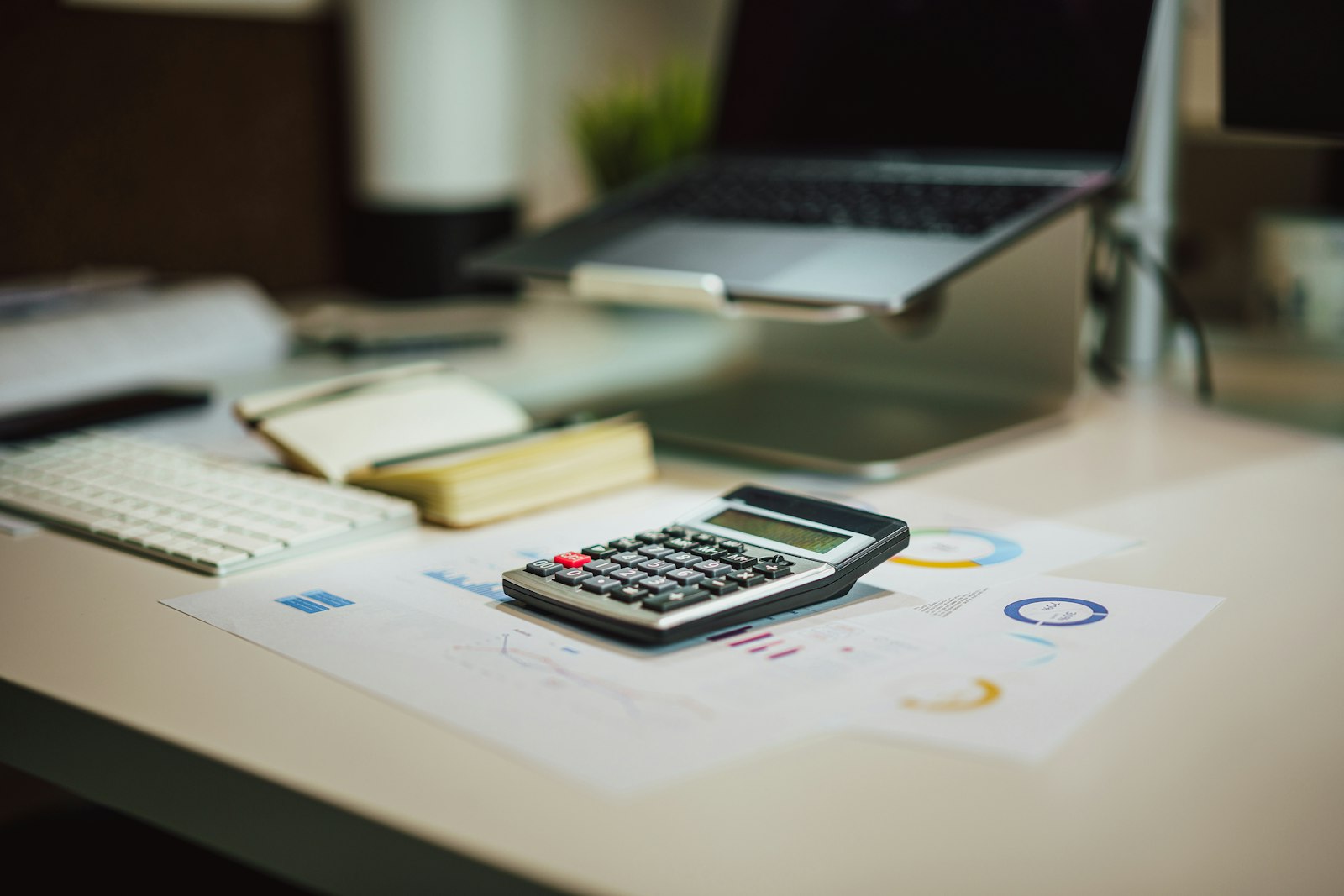 A calculator and paperwork on a desk next to a laptop
